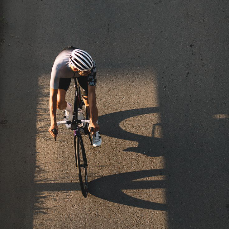 Rennrad Sportler von oben im Sonnenschein auf Asphalt.